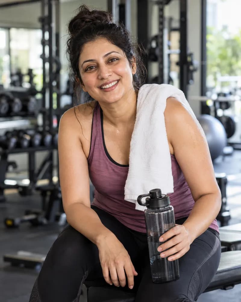 A smiling woman resting at the gym with a towel and water bottle